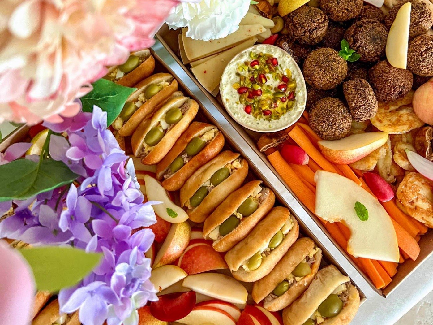 Buffet de plateaux apéritifs maison : fricassés, falafels, halloumi, crème de fêta, légumes croquants et fruits, entre des fleurs