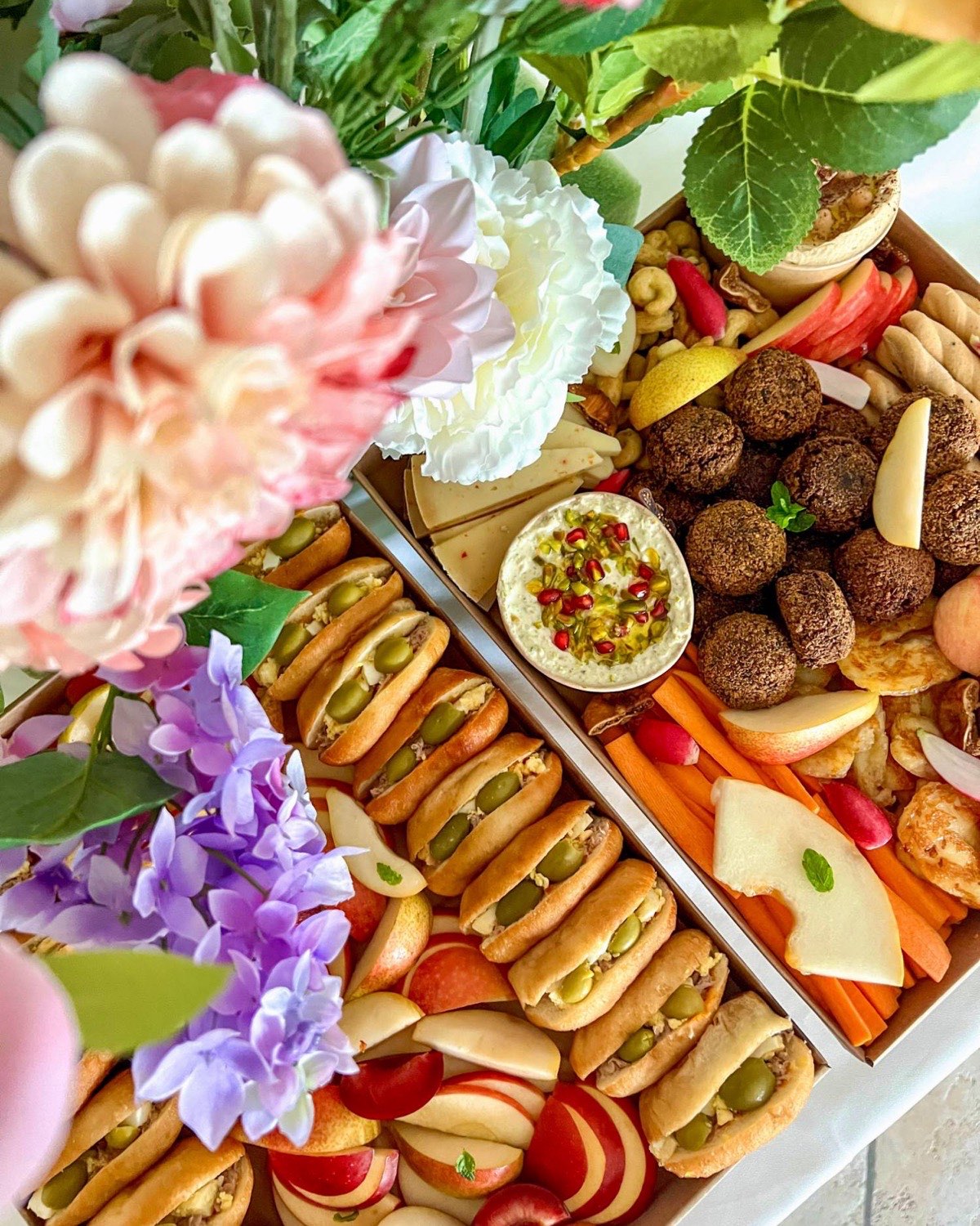 Buffet de plateaux apéritifs maison Entre L à Aix-en-Provence : fricassés, falafels, halloumi, crème de fêta, légumes croquants et fruits, entre des fleurs