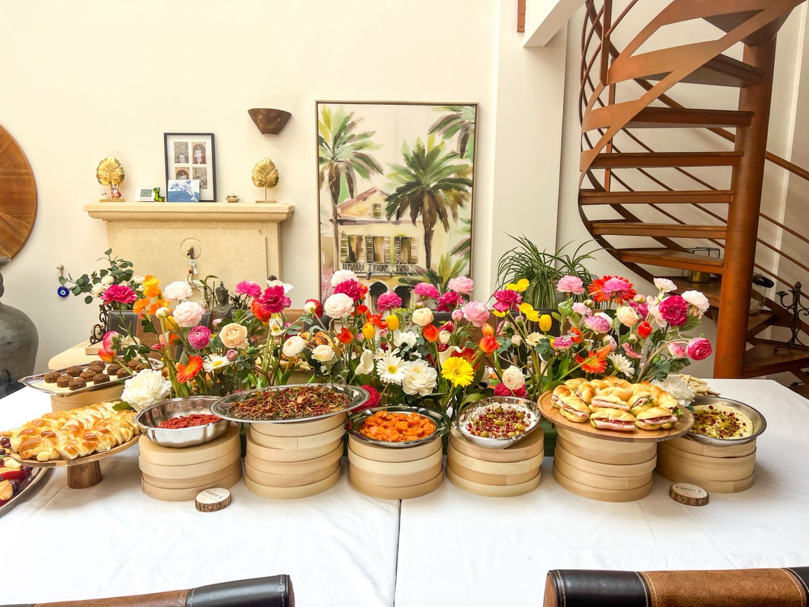 Buffet fait maison Entre L dressé dans un salon : hallah, mezzés, falafels et petits pains garnis, entre des fleurs