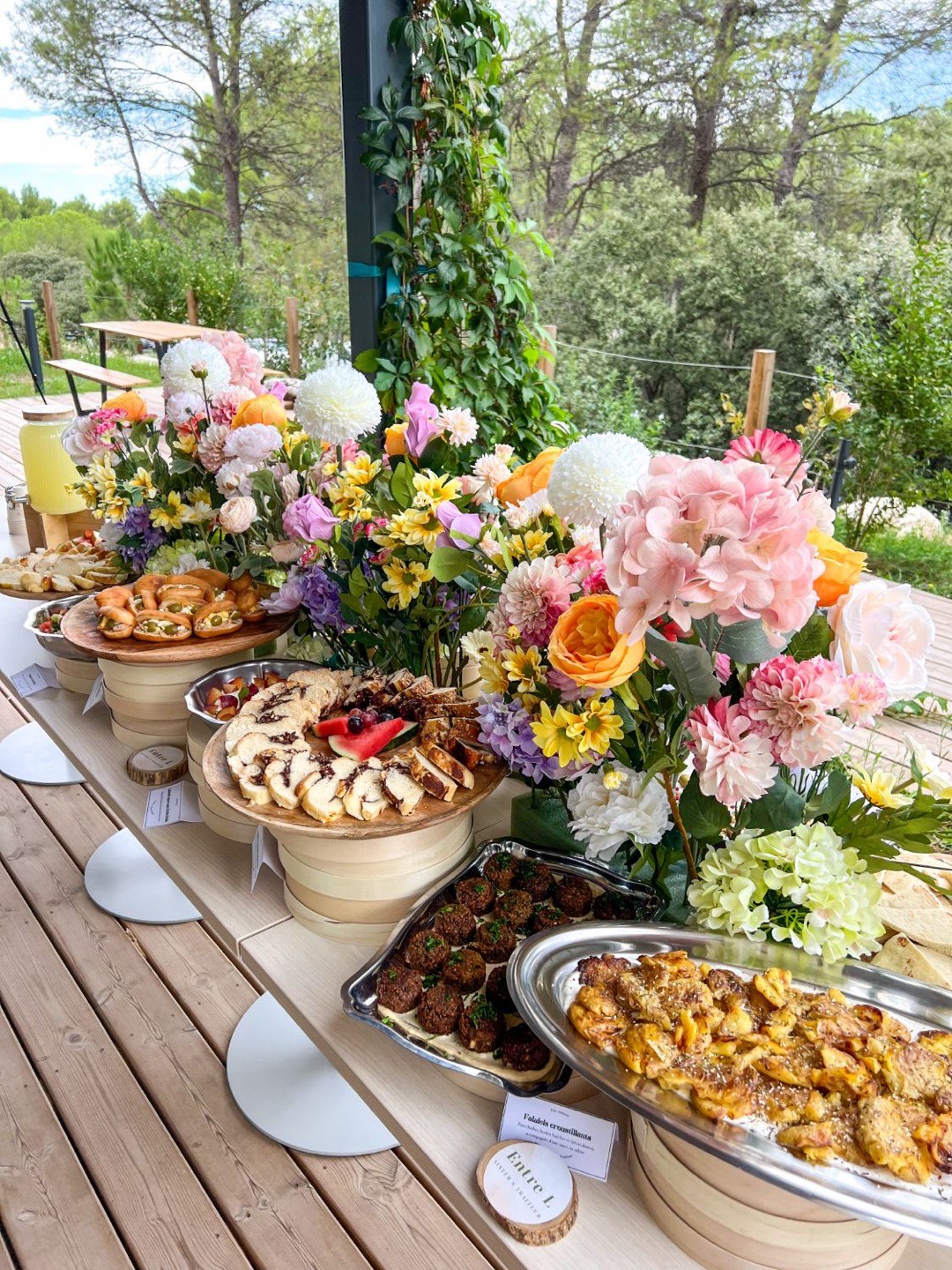 Buffet fleuri Entre L sur une terrasse en bois : falafels, babka, fricassés et pommes de terre rôties