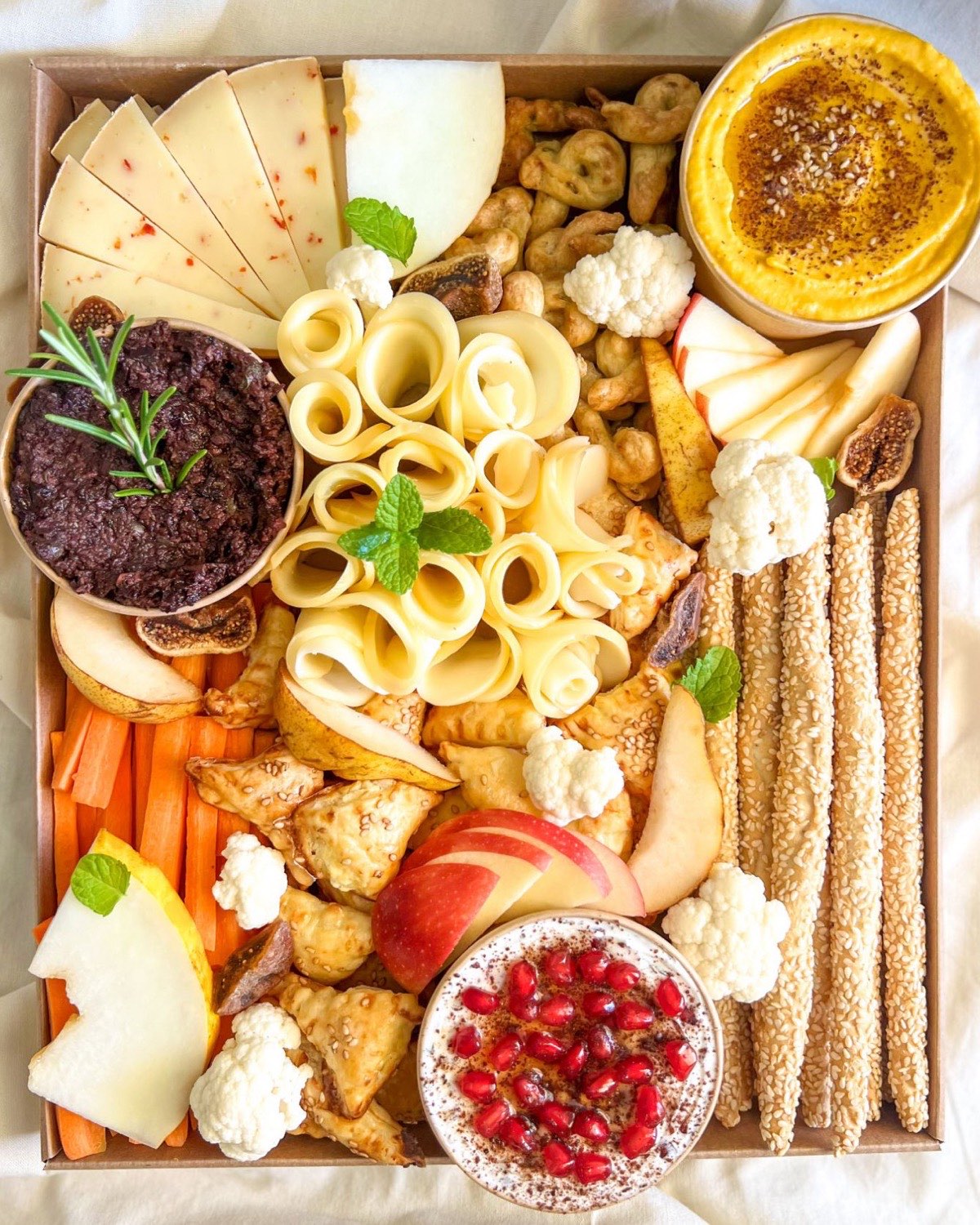 Plateau Grand Délices du Levant fait maison, vu de dessus : houmous de lentilles corail, labneh à la grenade, tapenade, burekas, fromages, agrumes et légumes de saison